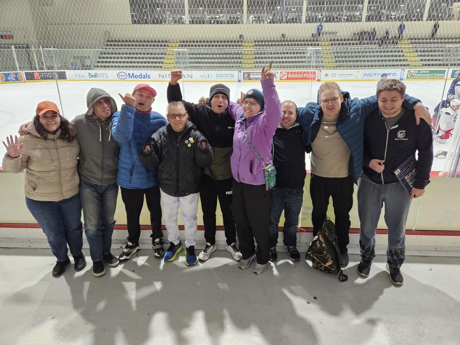 Nine participants standing arm in arm along the boards at a Winnipeg hockey rink