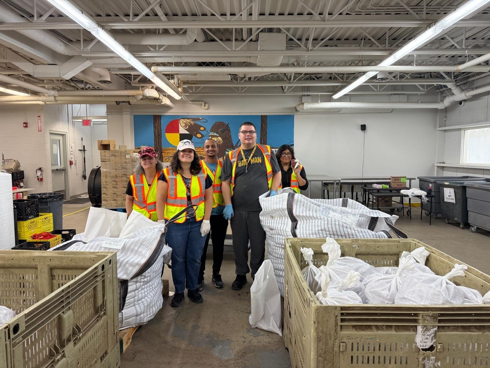 Five participants and staff in safety vests working together at a community food partner's warehouse