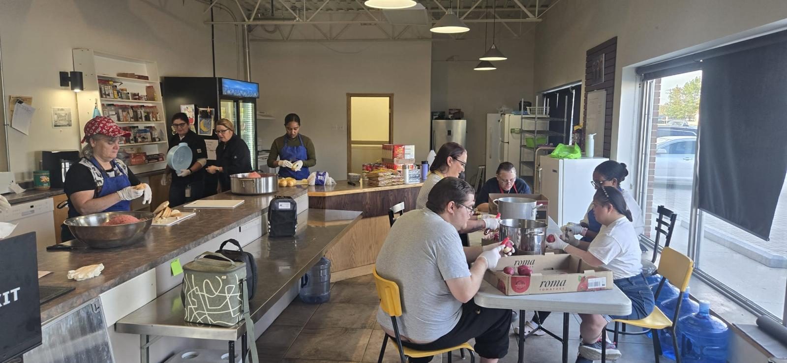 Participants and staff preparing vegetables together at the counters and tables of the EOW kitchen