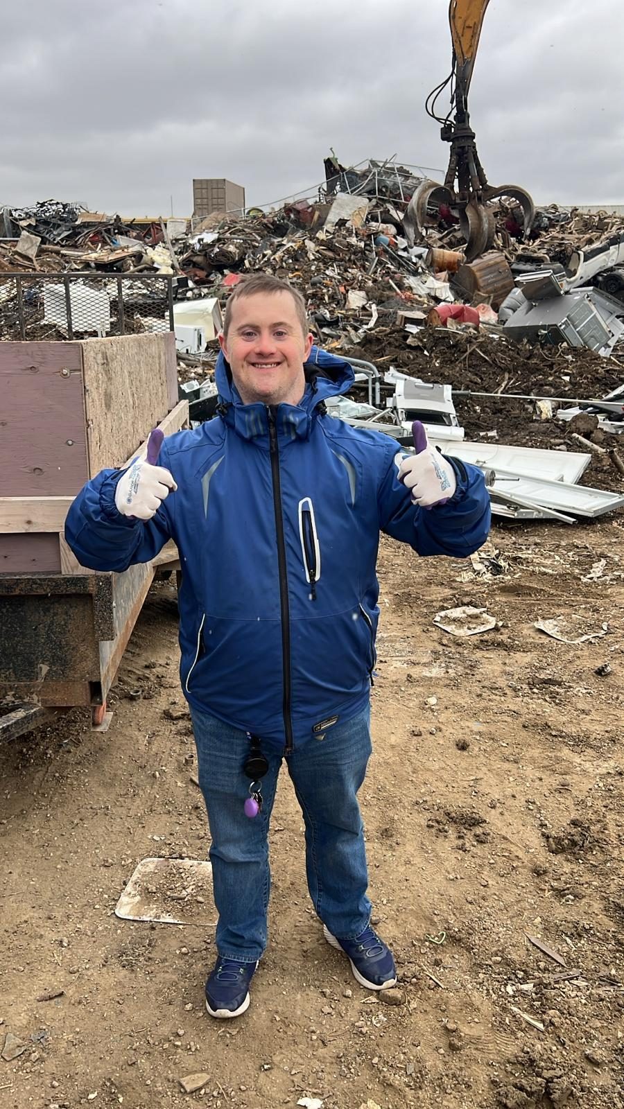 A participant in work gloves giving two thumbs up at the scrap metal yard where recovered materials are delivered